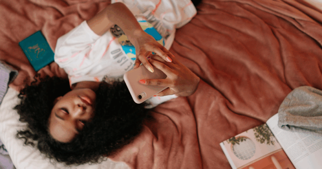 Teen using phone, lying on bed. Relatable image for articles on Hebephrenic Schizophrenia and mental health in young adults.