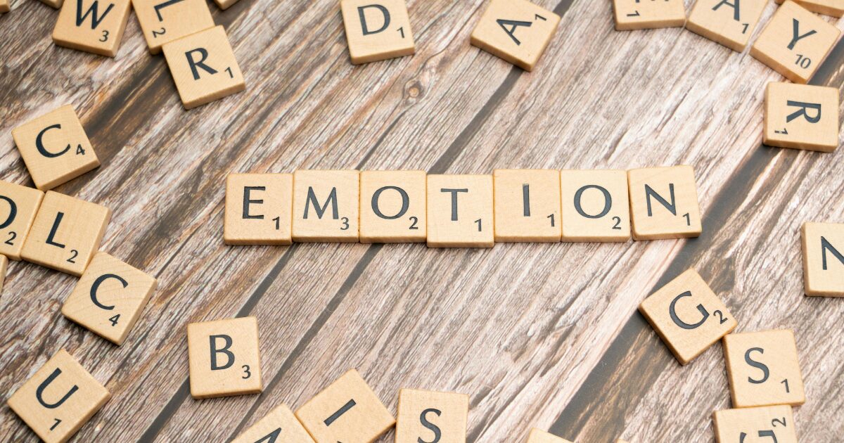 - Treat Mental Health Washington Scrabble tiles spelling EMOTION on a wooden table with scattered letters around.