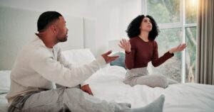 - Treat Mental Health Washington Man and woman sit on a bed in a bright bedroom, gesturing with their hands as they talk.