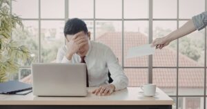- Treat Mental Health Washington Office worker in a white shirt at a desk, head in hand, as a hand offers a white envelope to him by a large window.