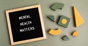 - Treat Mental Health Washington Black felt letter board reads 'MENTAL HEALTH MATTERS' beside green and yellow foam geometric shapes on a muted green background, conveying mental health awareness.