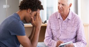 - Treat Mental Health Washington Young man sits with his head in his hands during a counseling session as an older man in a checkered shirt takes notes on a notepad